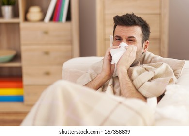 Man Blowing His Nose While Lying Sick In Bed