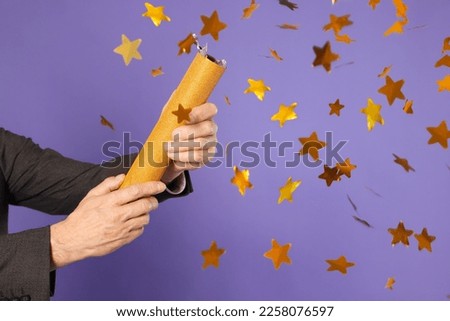 Man blowing up party popper on purple background, closeup