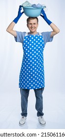 Man In Blue Apron, Rubber Gloves, Blue T-shirt, Jeans. Homeowner Holding A Basin With Dirty Laundry. Wash. White Background.