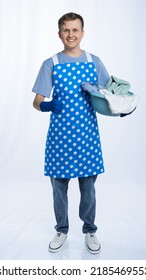 Man In Blue Apron, Rubber Gloves, Blue T-shirt, Jeans. Homeowner Holding A Basin With Dirty Laundry. Wash. White Background.