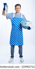 Man In Blue Apron, Rubber Gloves, Blue T-shirt, Jeans. The Homeowner Holds A Basin With Dirty Laundry And A Sock. White Background.