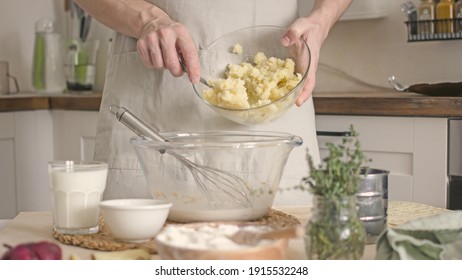 A Man In A Blue Apron, Without A Face, Prepares A Potato Dish In His Kitchen, Holds A Potato In His Hands And Peels It, Authentic Home Cooking. Male Home Cook Hobby