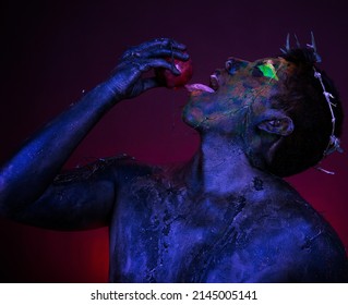 Man With Blue Body Paint And Apple On Red Background