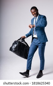 A Man In A Blue Business Suit With A Large Business Travel Bag Looks At His Watch And Hurries. Isolated On White Background.