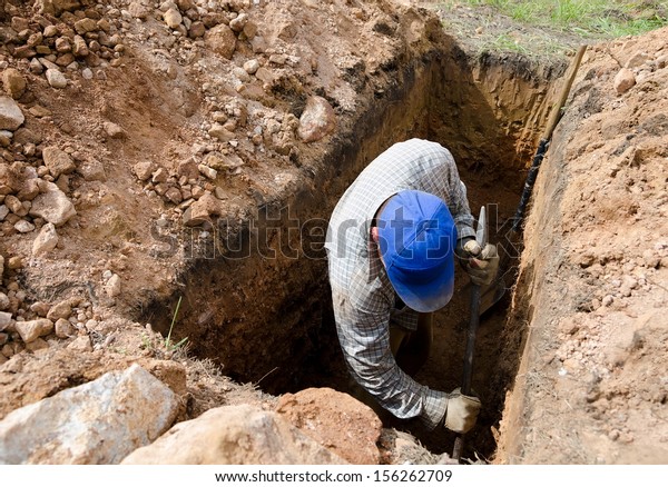 man in blue cap digs\
grave at cemetery