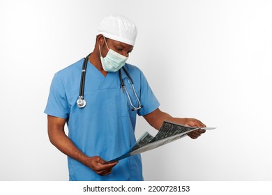 Man In Blue Coat White Cap And Surgeon Mask Holds X Ray Image Isolated On White Background. Pensive Adult African American Practicing Surgeon Portrait, Thoughtful Look