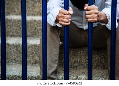 A man in blue collar shirt and black slacks behind the iron fence, Hand holding iron fence with a sense of hopelessness, sadness, solitude, sorrow, melancholy, quarantine and isolation. 