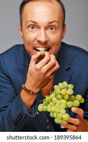 A Man In A Blue Jacket Eating Grapes