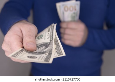 A man in a blue jumper holds money in his hands, a stack of 100 dollars blurred and close-up of money 100 dollars 200 dollars.Money concept