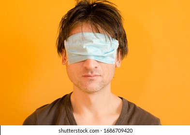 Man with blue mask on his eyes to not protect him from virus, on yellow background, epidemic coronavirus medical put on mask wrong concept. Tired man with uncombed hair on yellow background