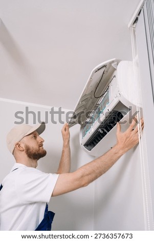 Man in blue overall checking ac appliances at home, performing seasonal maintenance. Concepts of installation and warranty service. Process replacing in air conditioning unit in a modern apartment