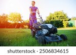 A man in blue overalls operates a lawnmower on a bright, sunny day, with a focus on the lawnmower in the foreground. The lush greenery and warm sunlight create an inviting, outdoor maintenance scene