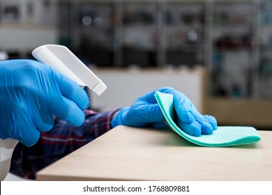 A Man In Blue Protective Gloves Disinfects The Surfaces Of An Audio And Video Equipment Store Using A Rag And Spray Disinfectant. Protection From Bacteria And Viruses.