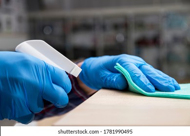 A Man In Blue Protective Gloves Disinfects The Surfaces Of An Audio And Video Equipment Store Using A Rag And Spray Disinfectant. Protection From Bacteria And Viruses.