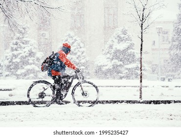 A Man In A Blue And Red Jacket Rides A Bicycle In Winter