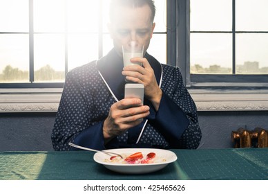 A Man In A Blue Robe, Eats Breakfast With Strawberry Yogurt With Phone In Hand