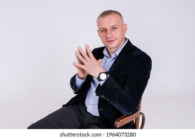 A Man In A Blue Shirt, Black Trousers And A Blue Jacket Sits On A Black Stool On A White Background