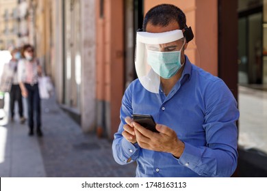 Man With Blue Shirt Face Mask And Plexiglass Screen Sends A Message With The Cellphone In The City Center