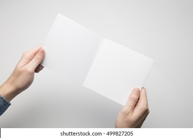 Man In Blue Shirt Is Holding A Square Bi-Fold White Paper Flyer.