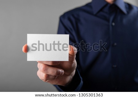 A man in a blue shirt holding a white business card