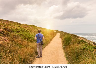 man in blue shirt on the edge of a long dirt road by the sea watching the sunset