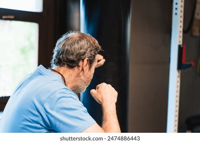 A man in a blue shirt practices martial arts by hitting a punching bag in a gymnasium. He wears a necklace and has a bald head. - Powered by Shutterstock