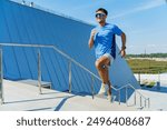 man in a blue shirt runs energetically up a modern staircase, with a vibrant blue building backdrop.