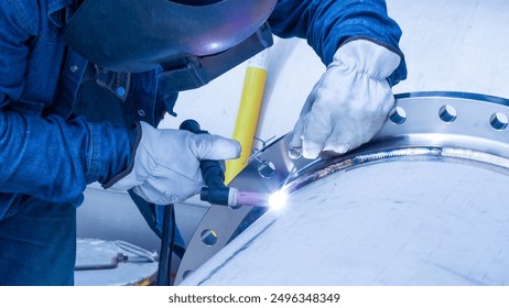 A man in a blue shirt is welding a pipe. Concept of hard work and dedication, as the man is focused on his task and using a torch to weld the pipe. The image also suggests a sense of danger - Powered by Shutterstock