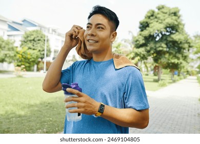 Man in a blue shirt wiping sweat from his face with a towel after an intense workout in a park - Powered by Shutterstock