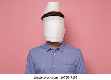 Man in blue shirt wrapped his face in a paper as medical mask trying to protect himself from coronavirus. Studio shot on pink wall.