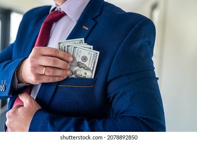 Man in blue suit and red tie putting bribe dollar bills into his pocket. corruption concept 