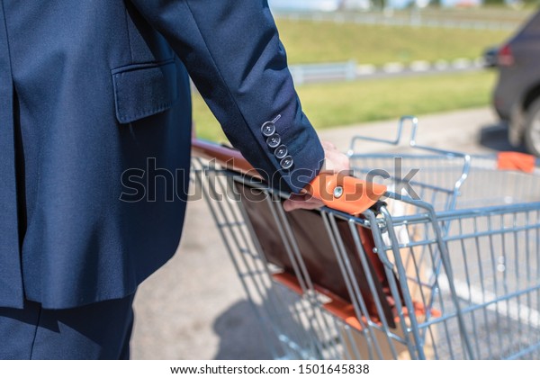 A man in a blue suit walks to\
his car with a supermarket trolley. Businessman and\
shopping