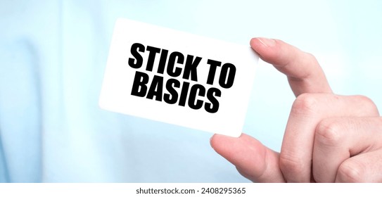 Man in blue sweatshirt holding a card with text STICK TO BASICS, business concept