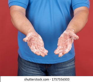 Man In A Blue T-shirt Holds His Hands In Front Of A Soapy White Foam, Body Hygiene Against Viral Diseases, Red Background