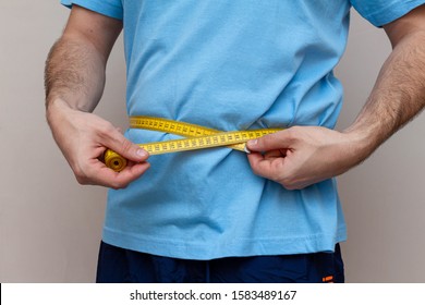 man in a blue T-shirt measures the waist with a yellow tape - Powered by Shutterstock