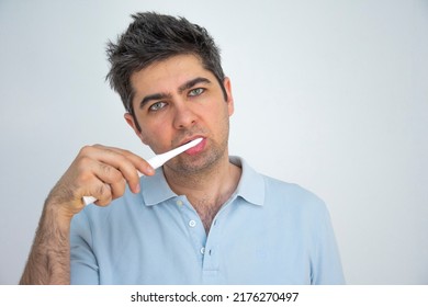 A Man In A Blue T-shirt With Tousled Hair Brushes His Teeth