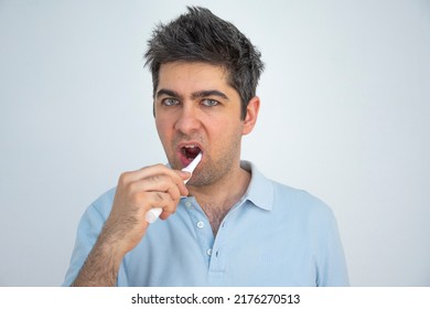 A Man In A Blue T-shirt With Tousled Hair Brushes His Teeth