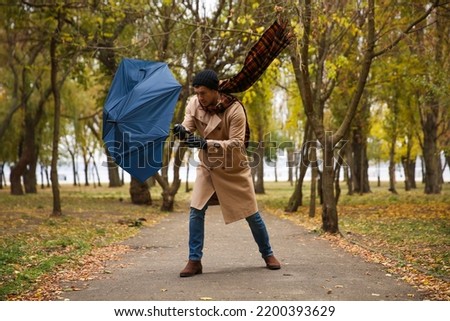 Man with blue umbrella caught in gust of wind outdoors