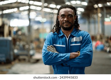 A man in a blue uniform stands in a factory with his arms crossed. He has a serious expression on his face - Powered by Shutterstock