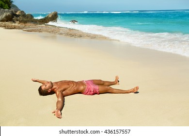 Man Body On Beach In Summer. Handsome Sexy Fit Male With Healthy Skin Sun Tan Tanning At Luxury Relax Spa Resort. Beautiful Fitness Model Relaxing, Sunbathing Lying On Sand. Summertime Travel Vacation