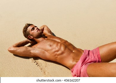 Man Body On Beach In Summer. Handsome Sexy Fit Male With Healthy Skin Sun Tan Tanning At Luxury Relax Spa Resort. Beautiful Fitness Model Relaxing, Sunbathing Lying On Sand. Summertime Travel Vacation