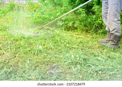 a man in boots mows the grass with a trimmer. the grass scatters