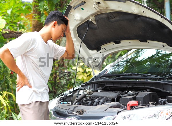 Man bored to\
check and repair interior the car,Asian man white shirt stand and\
feel bored about the engine of\
car