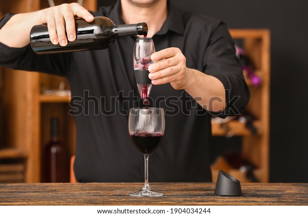 Man with\
bottle of wine, glass and aerator in\
cellar