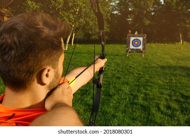 Man With Bow And Arrow Aiming At Archery Target In Park, Back View