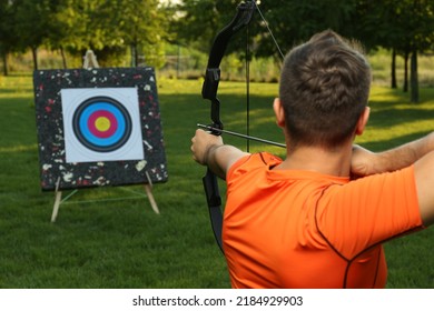 Man With Bow And Arrow Aiming At Archery Target In Park, Back View