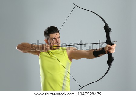Man with bow and arrow practicing archery on light grey background