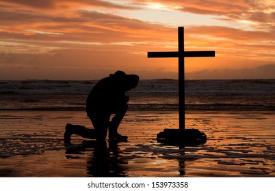 Man Bowing Down Before A Cross At Sunset.