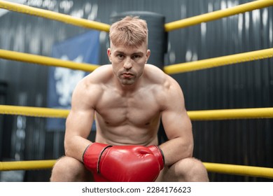 Man boxer sitting in corner on boxing ring at gym. Male MMA fighter looking competitor between rounds. - Powered by Shutterstock