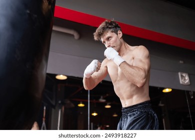 A man is boxing in a gym with a punching bag. He is wearing gloves and has a determined look on his face - Powered by Shutterstock